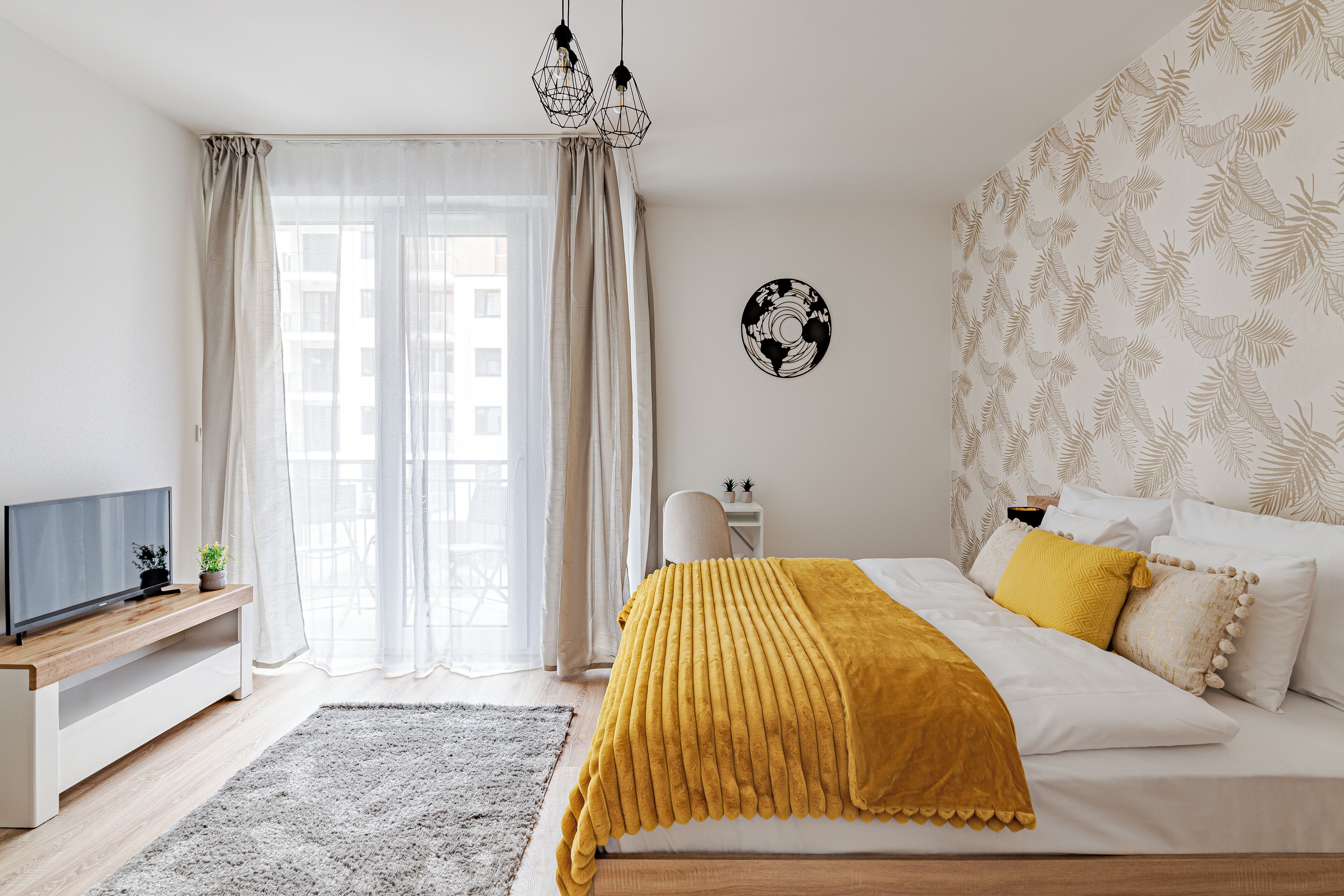 A bedroom with a bed, a TV, a desk, and a window with curtains.
