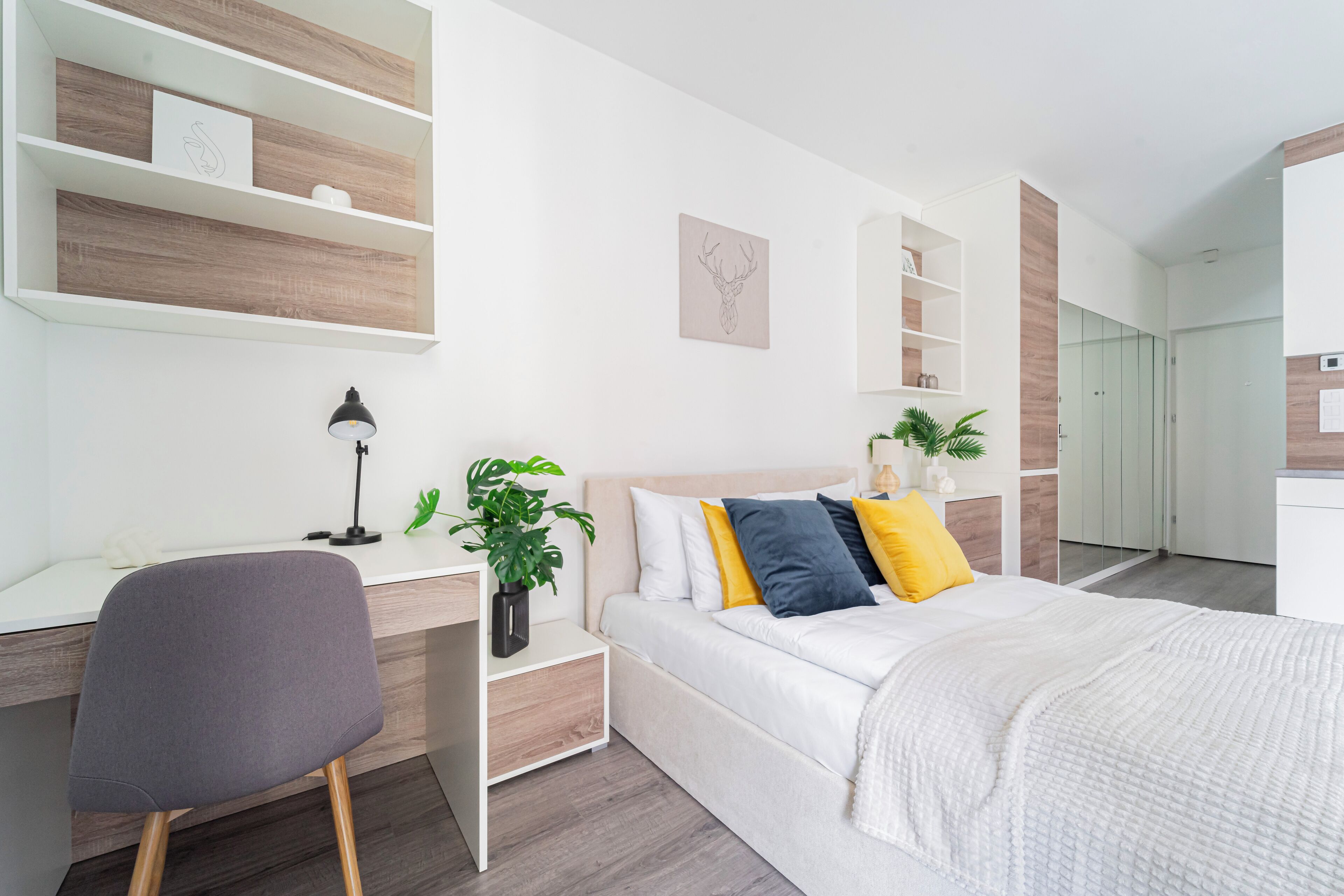 A modern bedroom with a bed, bedside table, desk, chair, and shelving unit.