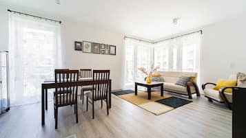 A modern living room with a dining area, featuring a sofa, chairs, a coffee table, and a TV.