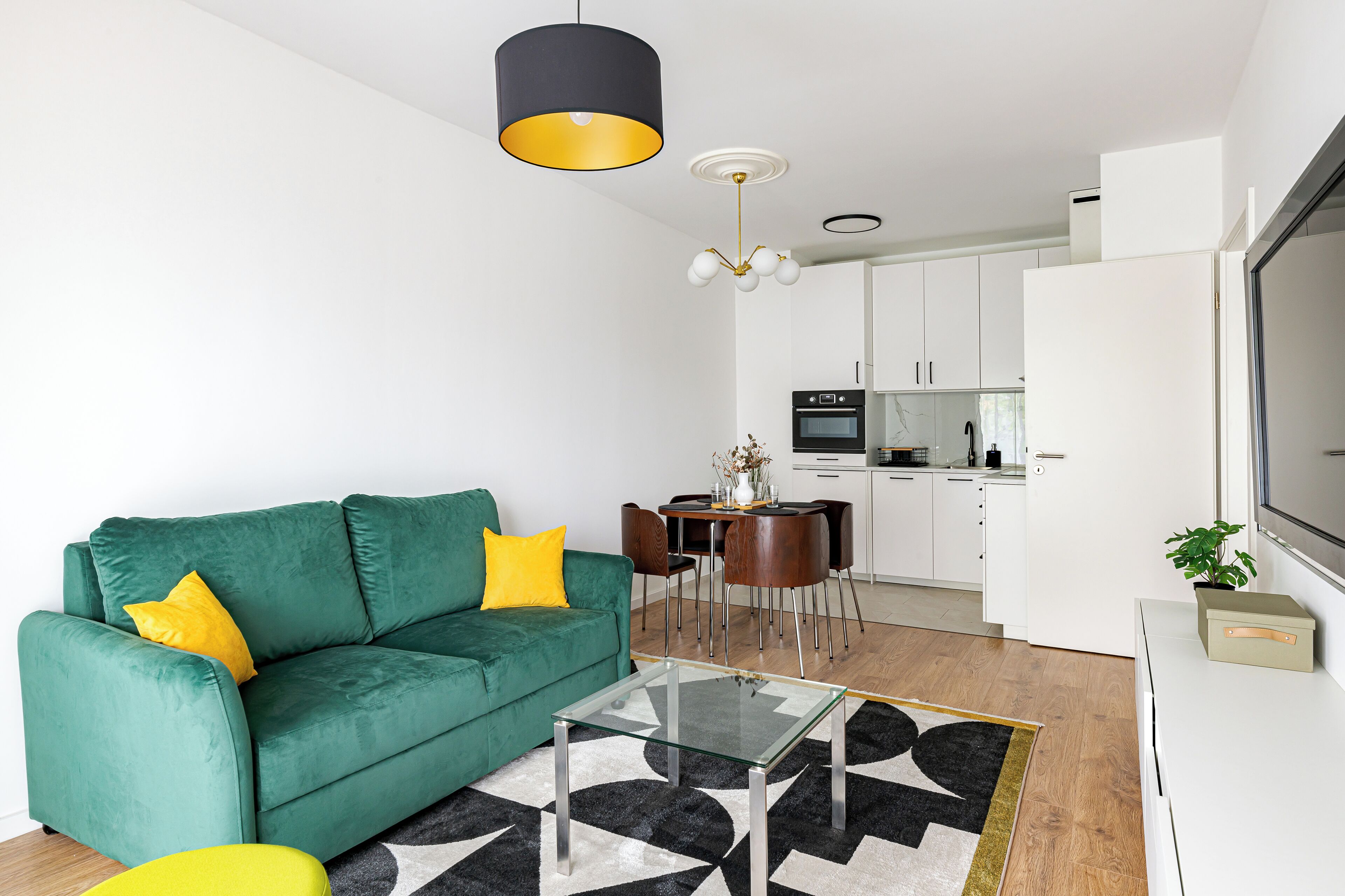 A modern living room with a green sofa, a glass coffee table, and a dining area with a white table and chairs.