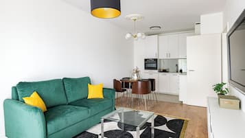 A modern living room with a green sofa, a glass coffee table, and a dining area with a white table and chairs.