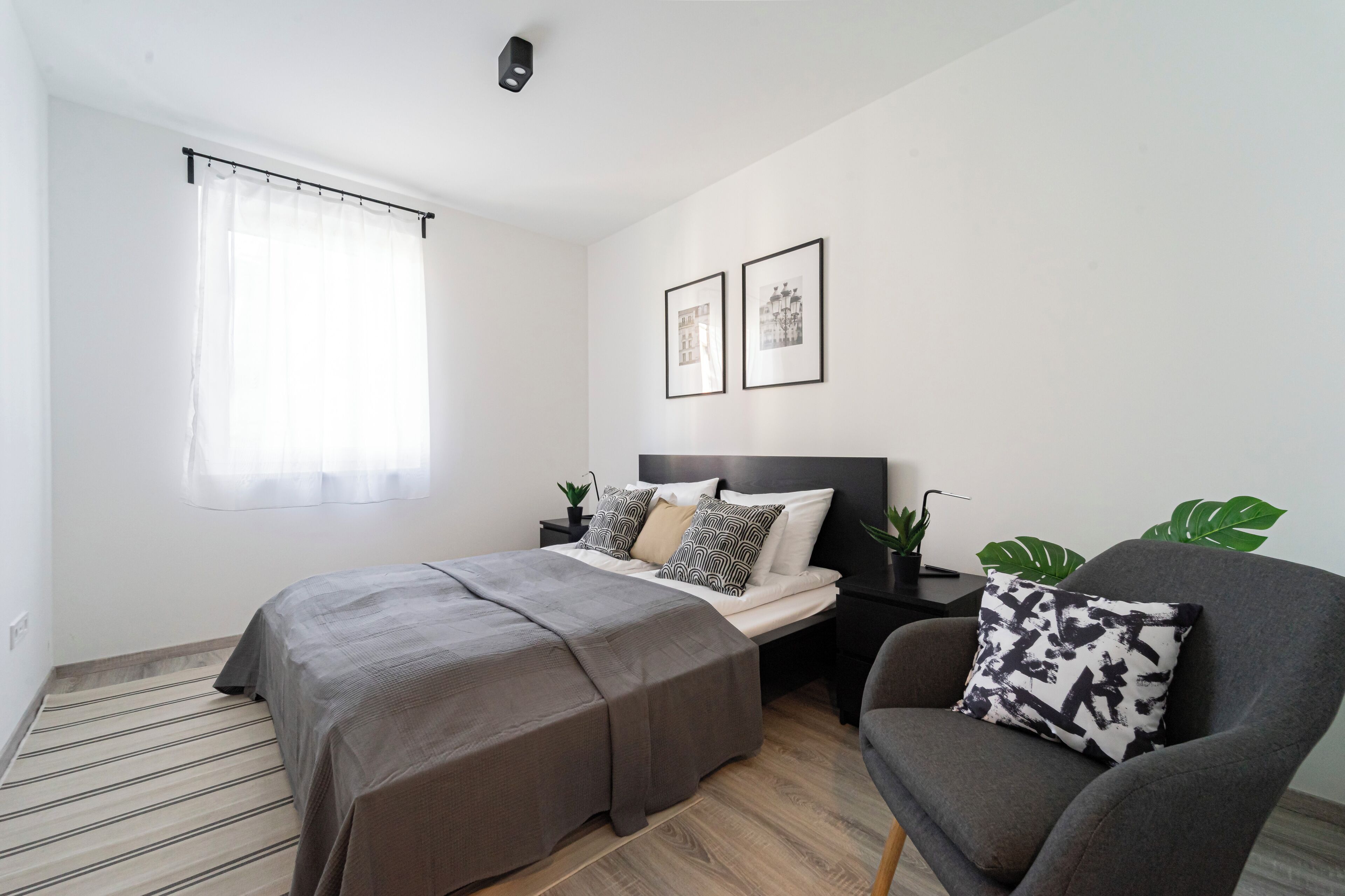 A bedroom with a bed, a chair, a nightstand, and a window with curtains.
