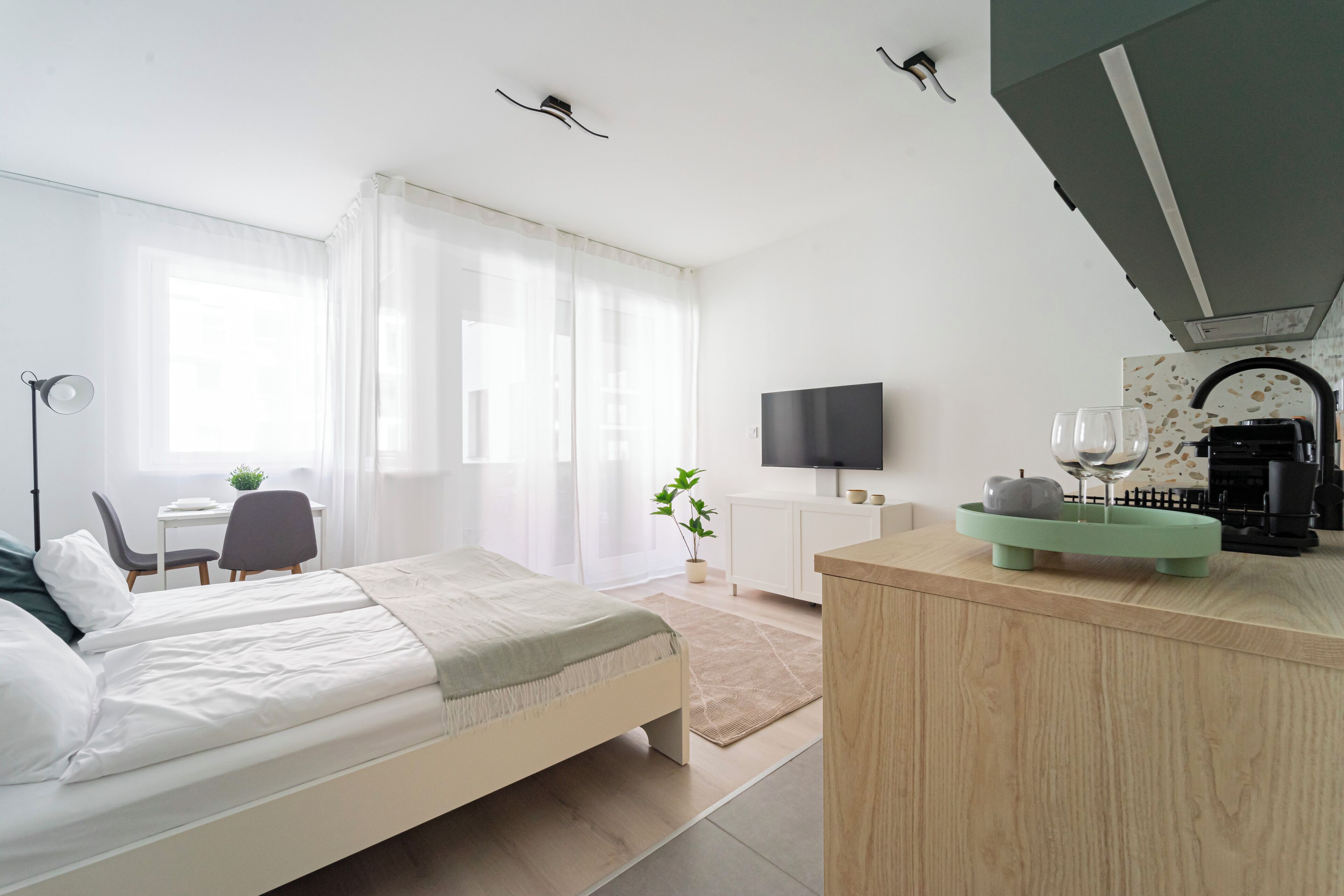 A modern hotel room with a bed, a desk, a TV, and a kitchenette.