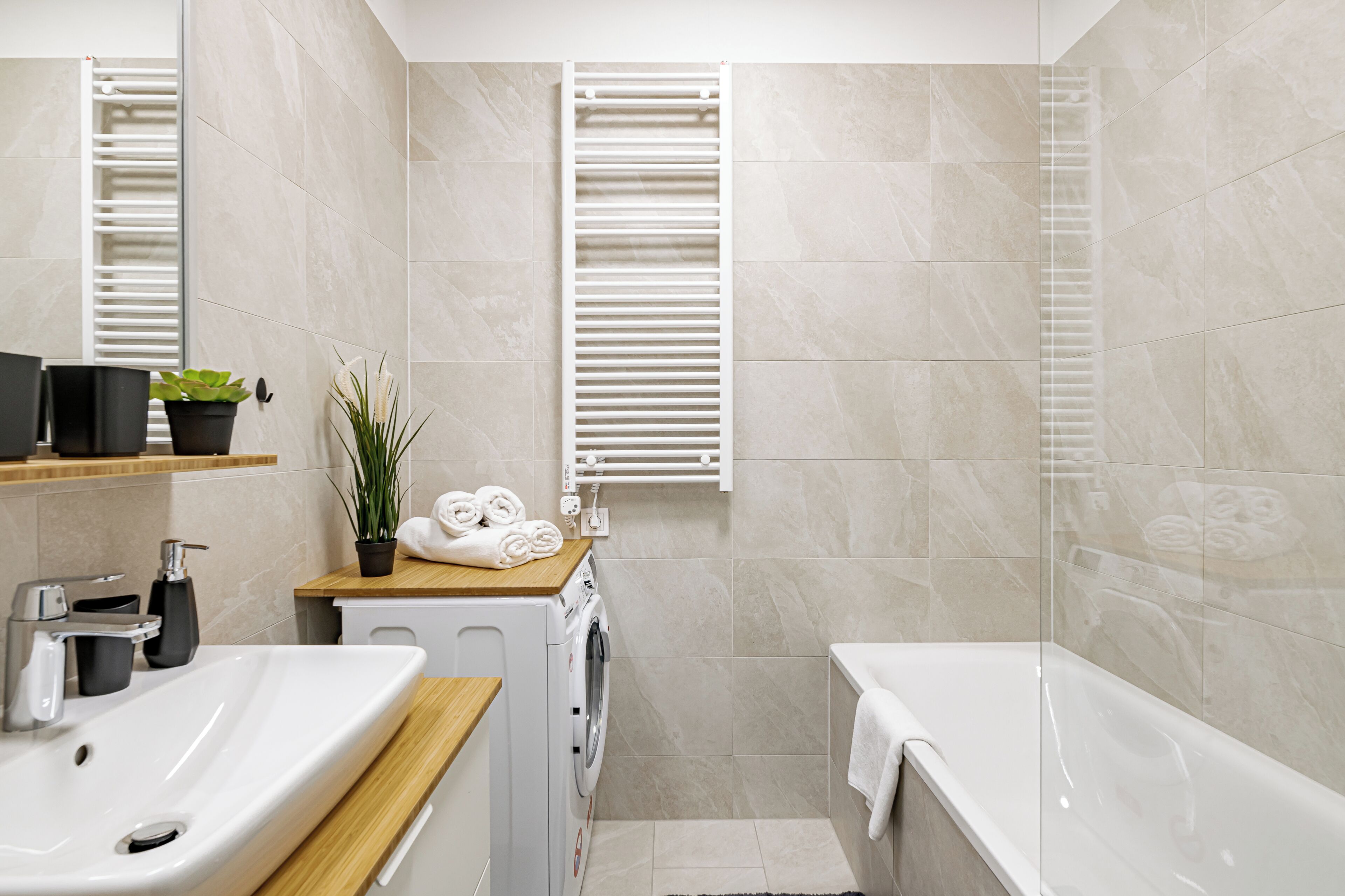 A modern bathroom with a sink, washing machine, and bathtub.