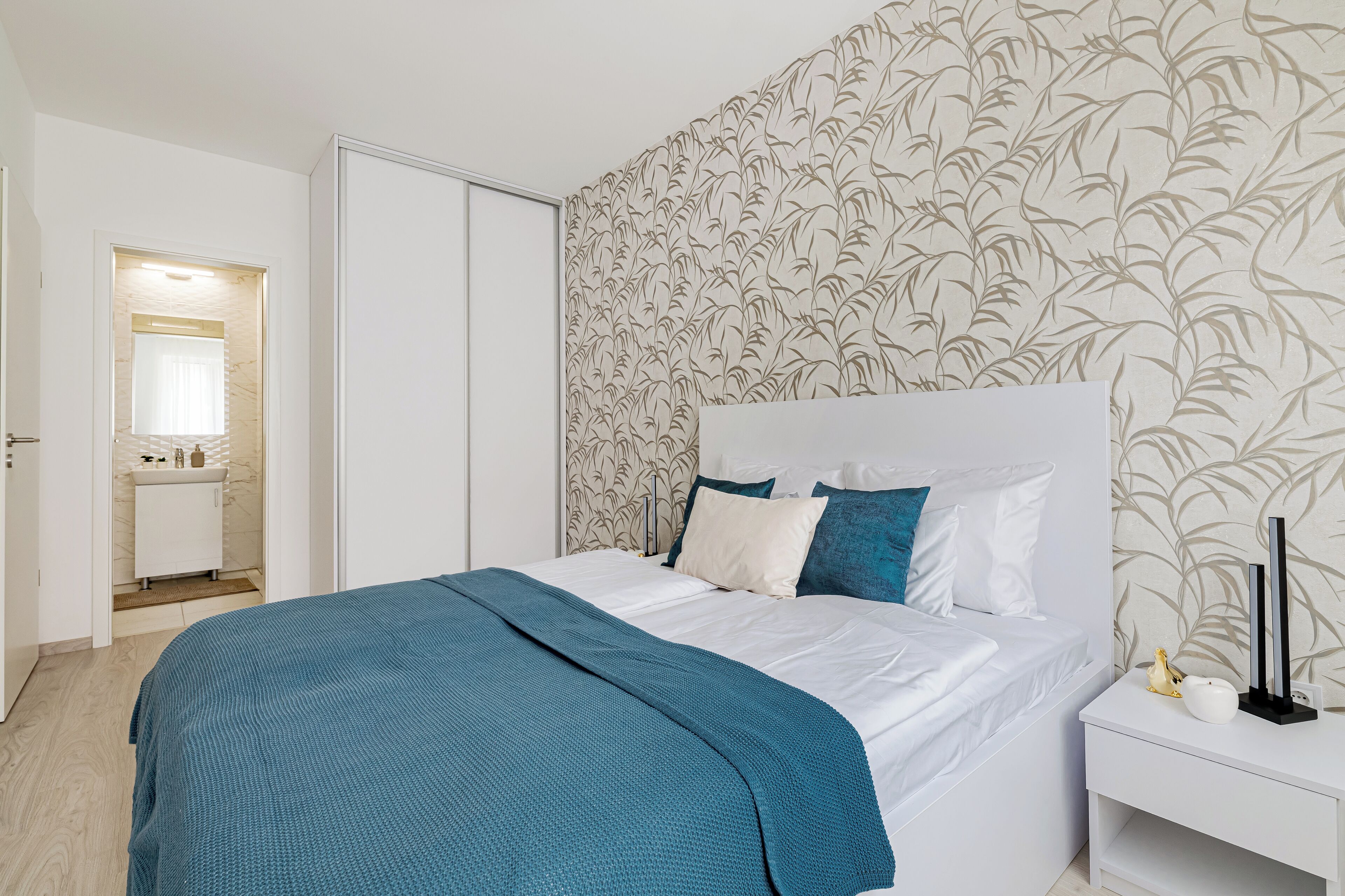 A bedroom with a bed, white nightstand, and a wall with a leaf pattern.