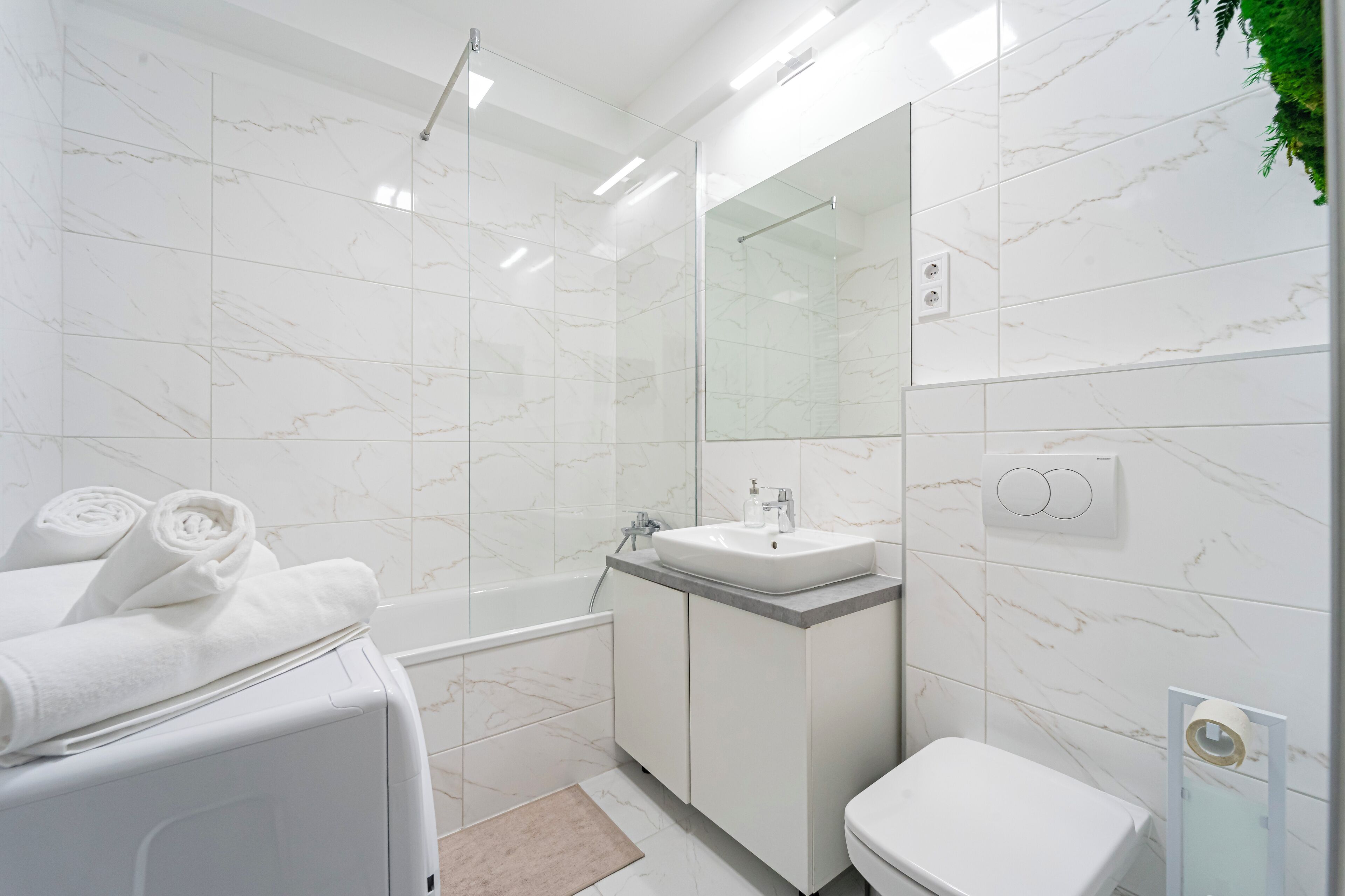 A modern bathroom with a white marble wall, a glass shower enclosure, a white sink, and a toilet.