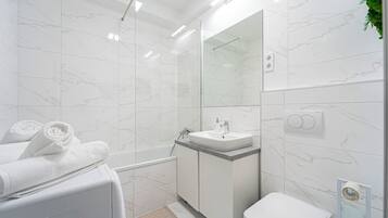 A modern bathroom with a white marble wall, a glass shower enclosure, a white sink, and a toilet.