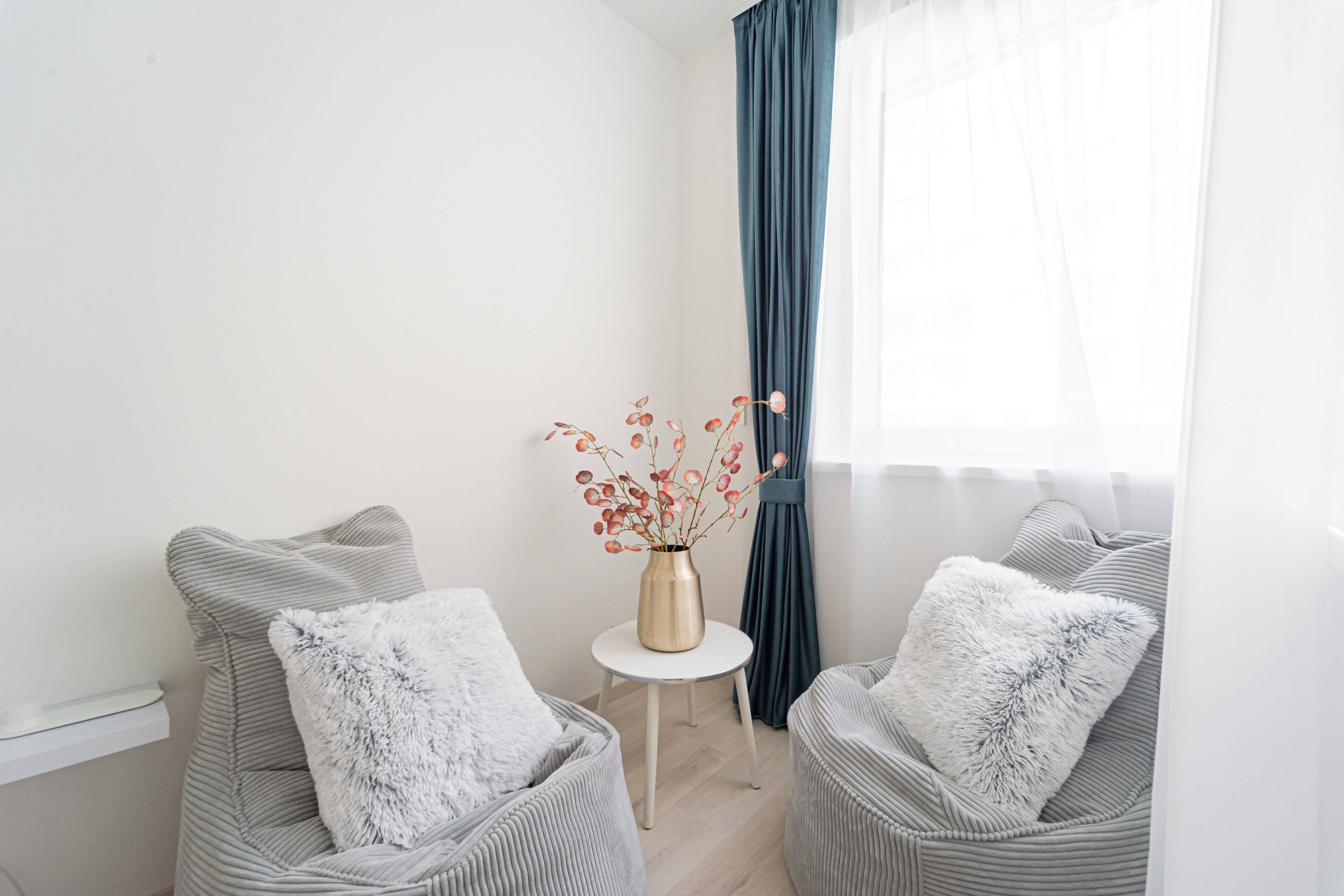 A modern room with two grey upholstered chairs, a small white table, and a vase with red flowers.