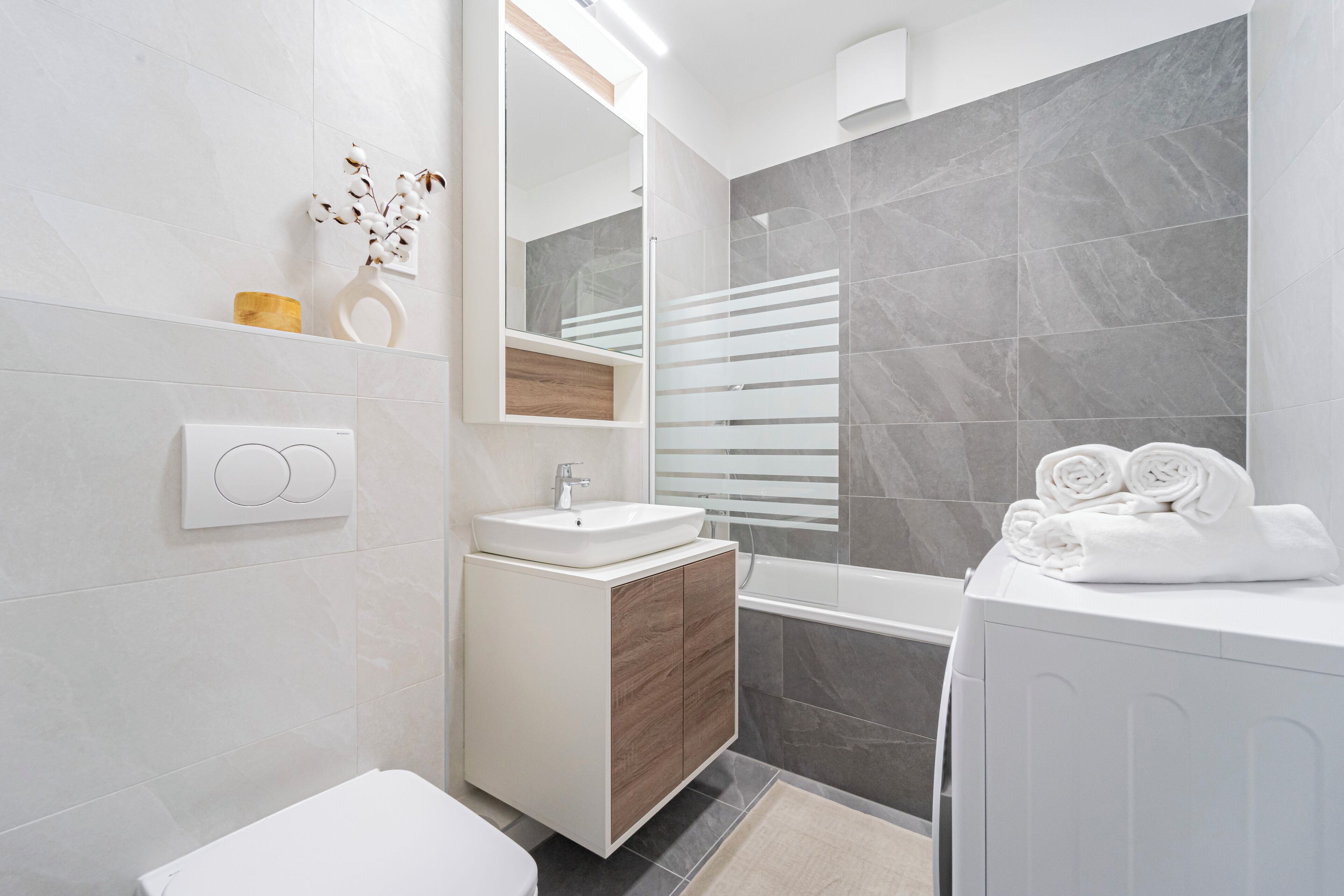 Een moderne badkamer met een witte wastafel, houten opbergmeubel, een spiegel en een bad.