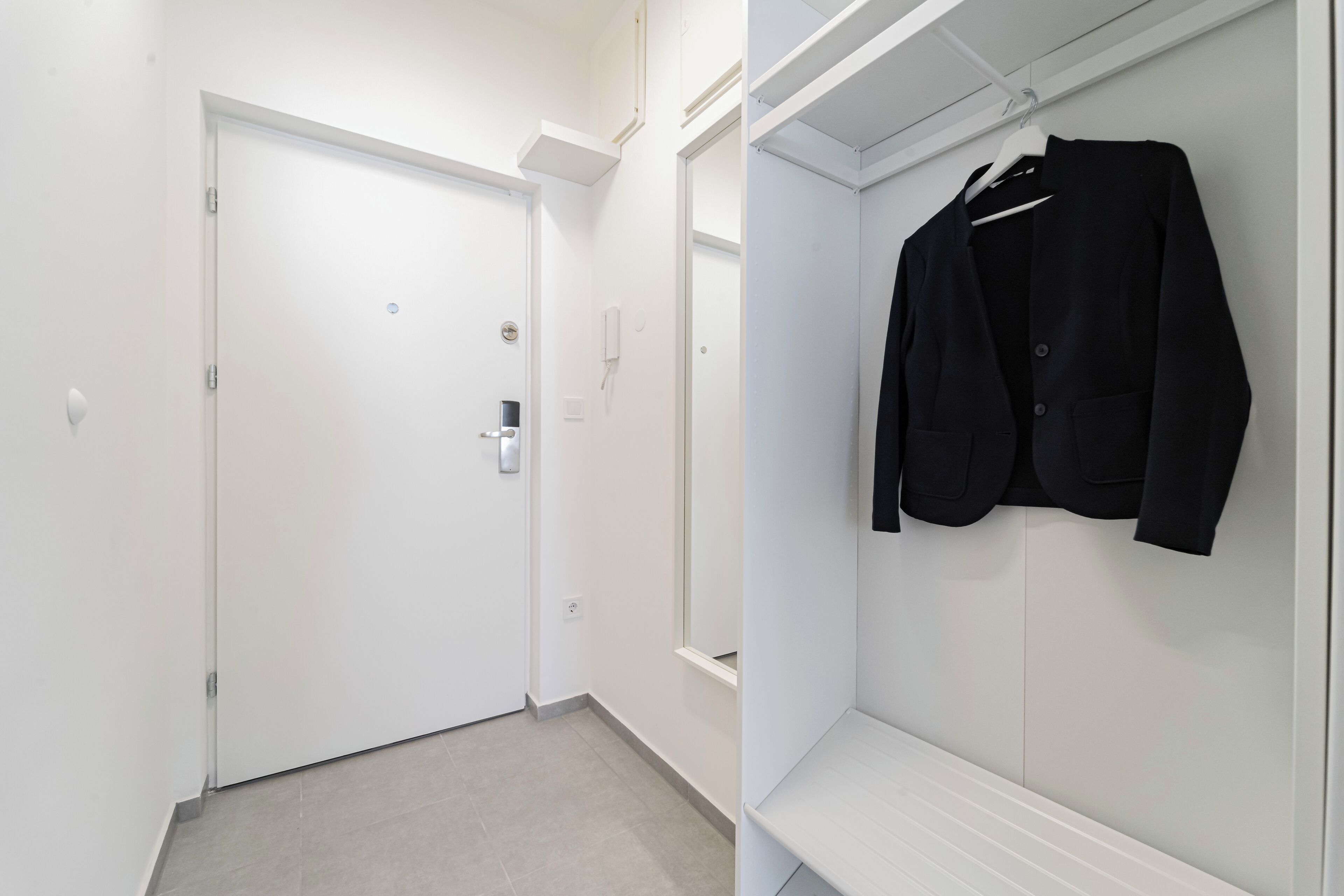 A hallway with a white door and a closet with a hanging coat rack.