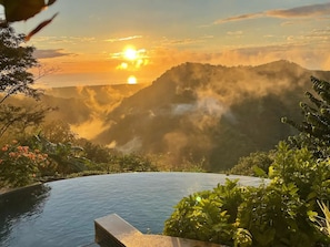 A pool with a view of a sunset over misty mountains.
