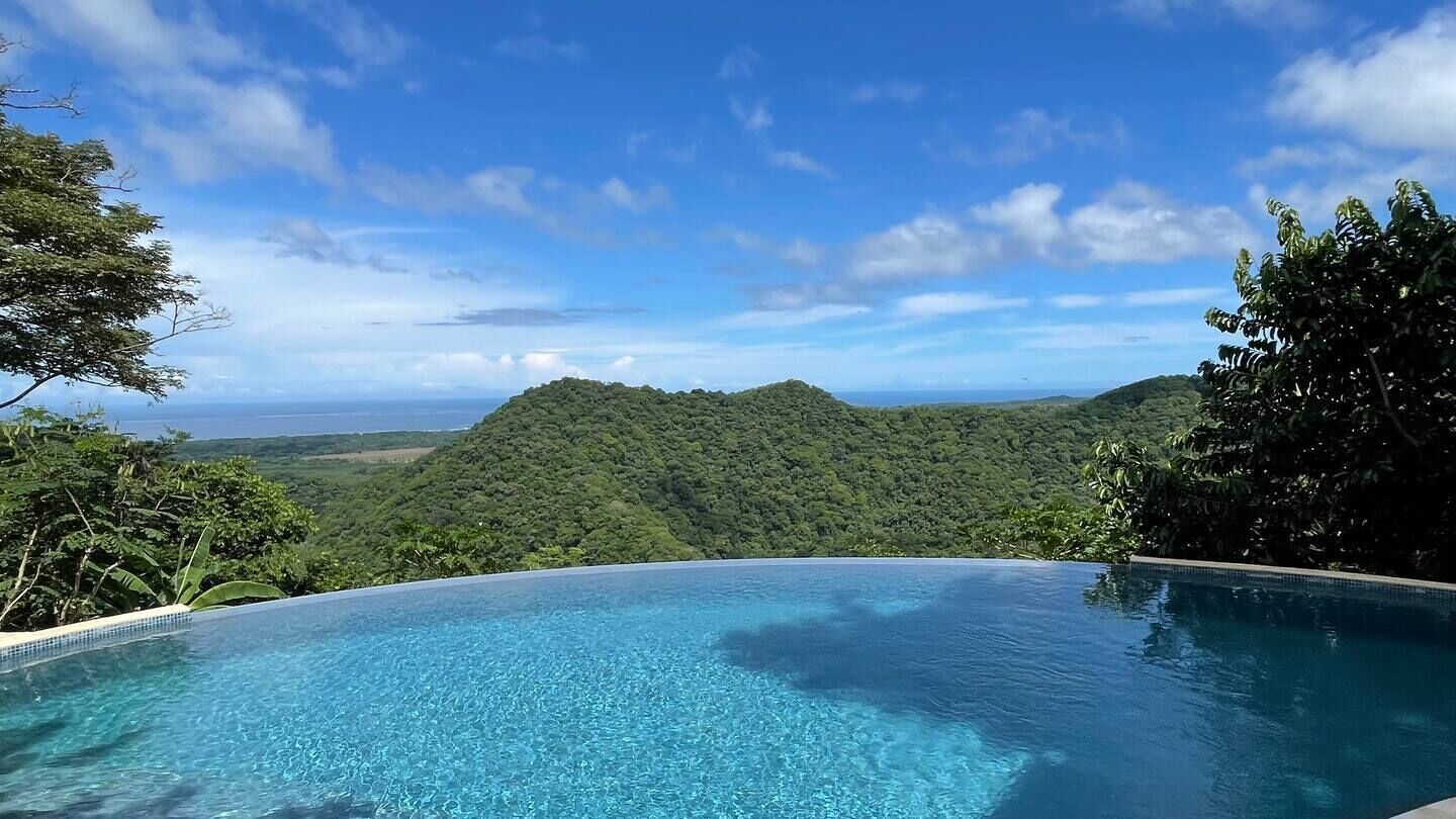 An infinity pool with a view of a lush green mountain and the ocean.