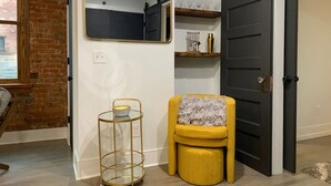 A room with a large mirror, a small round table with a candle, a yellow chair, and a dark door. - Timeless Loft -OTR -TQL w/ FREE Parking (Cincinnati)