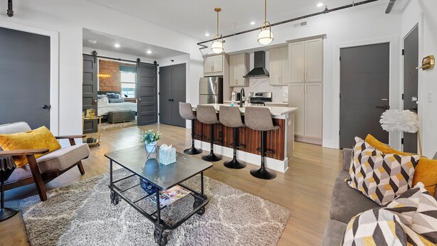 A modern living room with a coffee table, sofa, and a dining area with bar stools. - Timeless Loft -OTR -TQL w/ FREE Parking (Cincinnati)