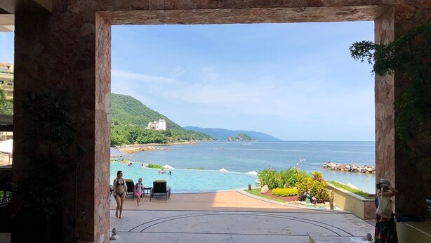 Blick vom Balkon auf Pool und Strand, mit blauem Himmel und ferner Hügelkette.