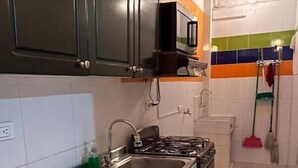 A kitchen with dark cabinets, a gas stove, a sink, and a microwave. There is a broom and mop in the background.