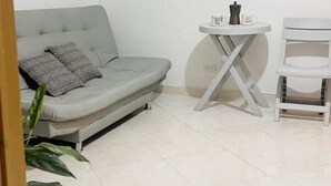 A small, clean room with a grey sofa, a small table, and a chair.
