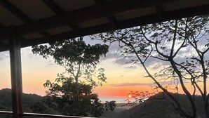 Une terrasse en bois avec un jacuzzi, offrant une vue sur un paysage boisé au coucher du soleil.