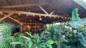 Une construction rustique en bois, dotée d’un toit de chaume, entourée d’une végétation tropicale luxuriante.
