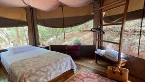 Une tente avec un lit, un tapis rouge à motifs et un banc en bois.