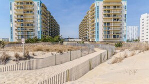 A beachfront hotel with multiple balconies, a sandy beach in the foreground, and a clear sky. - Direct Oceanfront Condo with Ocean and Bay Views (Ocean City)