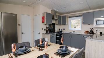 A modern kitchen with grey cabinets, a stainless steel refrigerator, and a dining area with a wooden table set for four.