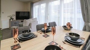 A modern living room with a dining area. It includes a sofa, a television, and a dining table set with copperware and black bowls.
