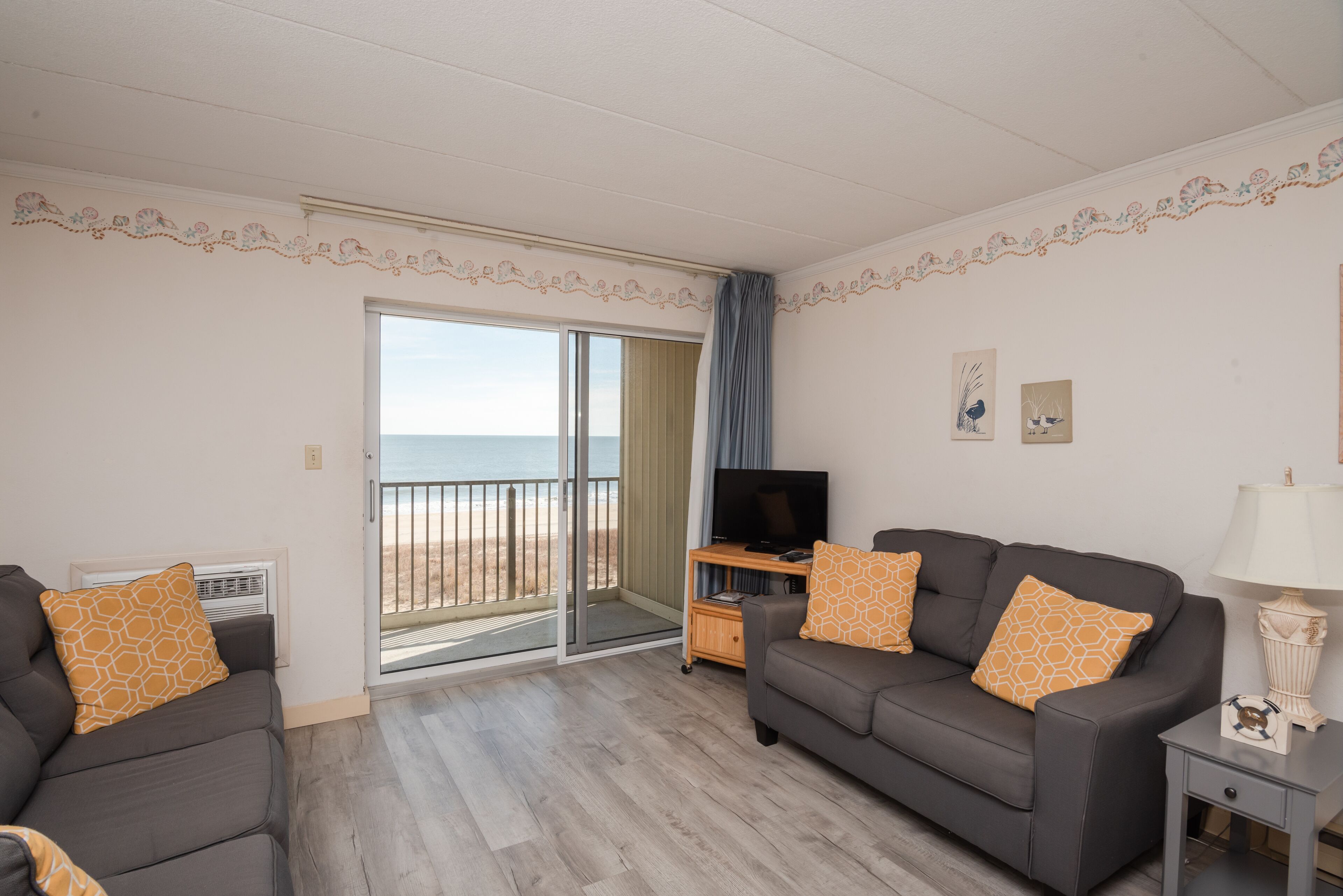 Un salon avec un canapé, une télévision et une vue sur la plage, accessible par une porte coulissante.