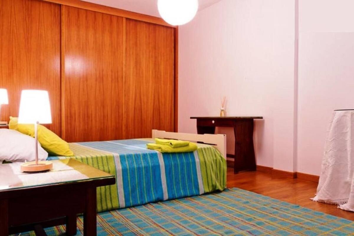 A bedroom with a bed, bedside table, lamp, and a small desk.
