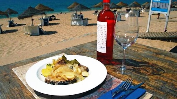 A beachside dining table with a plate of food, a wine bottle, and a glass.
