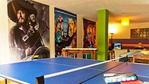 A ping pong table with paddles and a table tennis ball, a TV, and posters on the wall.