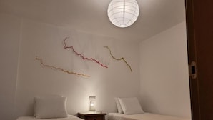 A bedroom with two beds, a bedside table with a lamp, and abstract wall art.