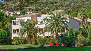 A multi-story residential building with balconies, surrounded by lush greenery and palm trees. - L'Anse de Pramousquier, T2 Vue Mer ! Bord de plage (Le Lavandou)
