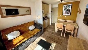 A compact living space with a sofa, a dining table with chairs, a kitchen area, and a TV mounted on the wall. - L'Anse de Pramousquier, T2 Vue Mer ! Bord de plage (Le Lavandou)
