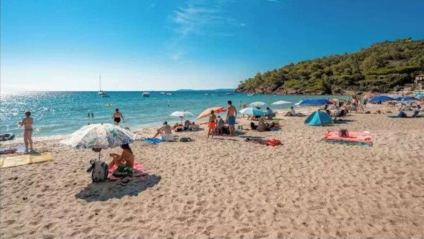 A beach with people sunbathing, umbrellas, and a sailboat in the distance. - L'Anse de Pramousquier, T2 Vue Mer ! Bord de plage (Le Lavandou)