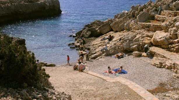 A rocky beach with people relaxing and a clear view of the sea.