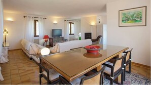 A modern hotel room with a dining area, a sofa, a TV, and a fireplace.