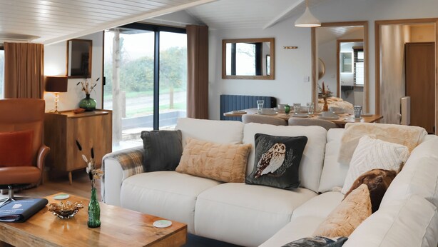 A modern living room with a white sofa, wooden coffee table, and a dining area with a table set for two.