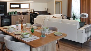 A modern living room with a dining area, a sofa set, a kitchen with a washing machine, and a large window with curtains.