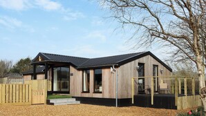 A modern wooden house with a covered porch, a fenced yard, and a gravel driveway.