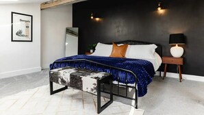 Ein Schlafzimmer mit einem Bett, einem Nachttisch, einer Lampe, einer Bank und einem Poster an der Wand.