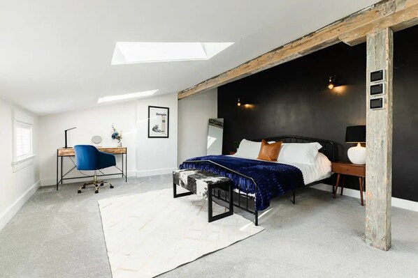 Une chambre moderne avec une lucarne, un lit recouvert d’une couette bleue et blanche, un bureau avec une chaise et une table de chevet avec une lampe.