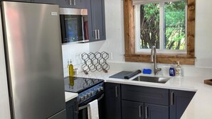 A modern kitchen with dark cabinets, stainless steel appliances, a window with a wooden frame, and a tiled floor.