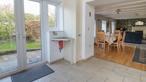 A modern kitchen with a dining area, a stone fireplace, and a view of the garden. - Tegfan (Newport)