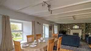 A dining area with a round table set for four, wooden chairs, and a checkered tablecloth. There is a stone fireplace in the background and a blue sofa in the living area. - Tegfan (Newport)