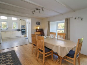A dining area with a table set for four, wooden chairs, a patterned rug, and a kitchen in the background. - Tegfan (Newport)