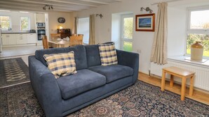 A living room with a blue sofa, a patterned rug, a wooden table, and a view of the kitchen and dining area through a window. - Tegfan (Newport)