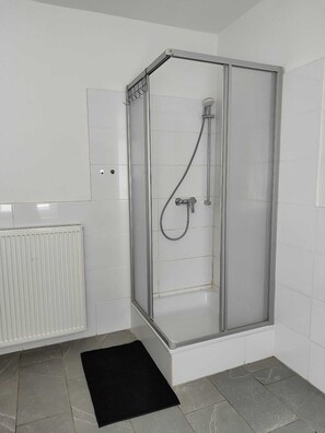A modern bathroom with a glass-enclosed shower, white tiles, and a black rug.