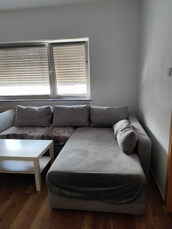 A modern living room with a grey sectional sofa, a small white table, and a window with blinds.