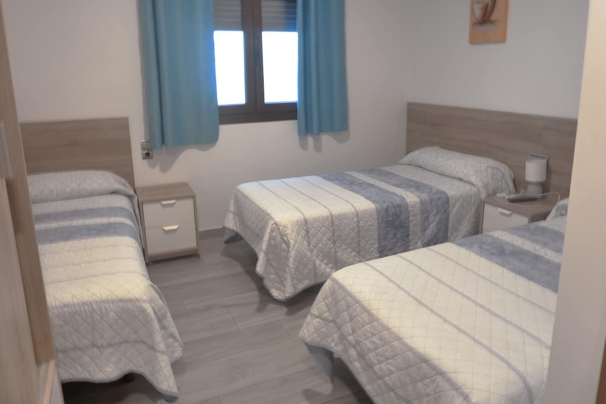 Ein Schlafzimmer mit zwei Einzelbetten, einem Nachttisch mit Lampe und einem Fenster mit Vorhängen.